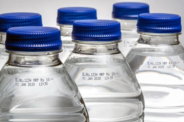 Clear PET bottles with blue caps showing CIJ batch and date coding.
