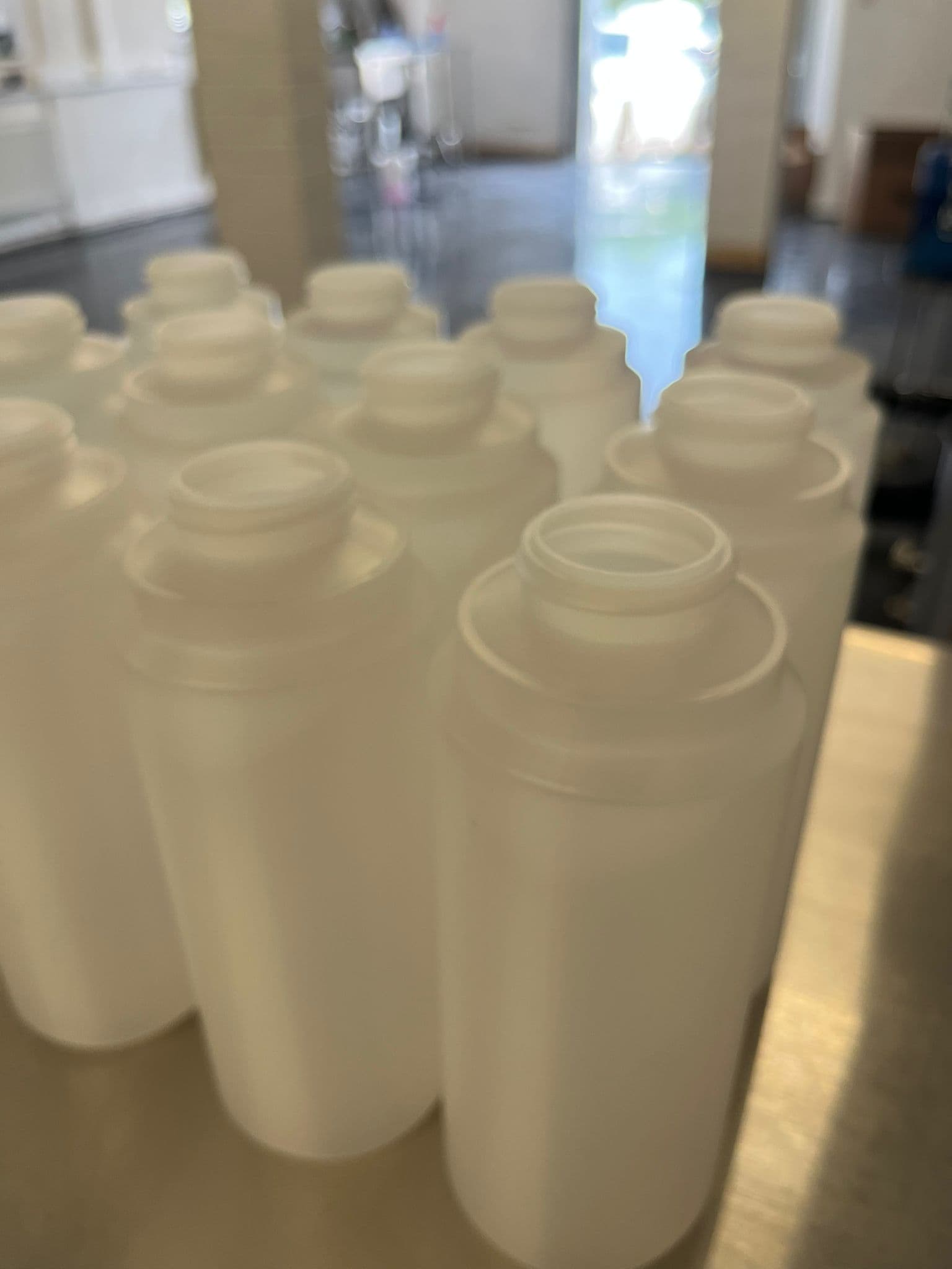 Empty food-grade HDPE bottles staged on a stainless bench before filling.