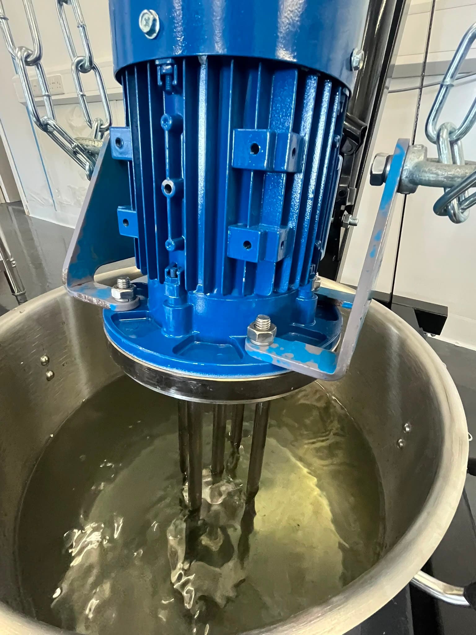 Blue high-shear motor over a stainless mixing vessel with amber liquid.
